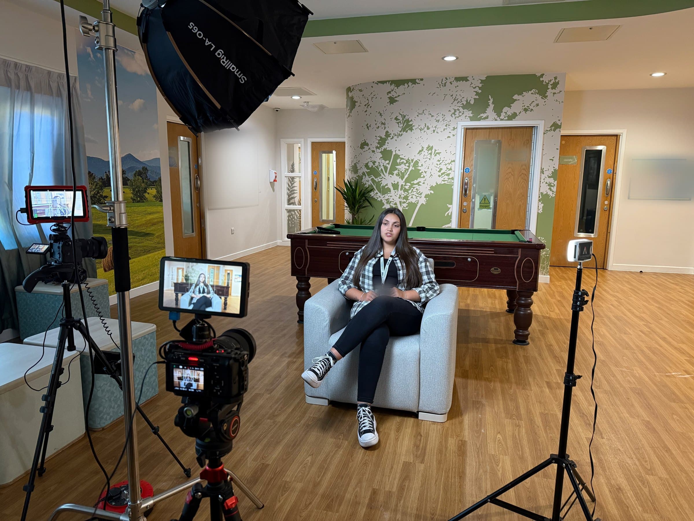 An Expert by Experience sitting in an armchair in front of cameras and lights, being filmed.