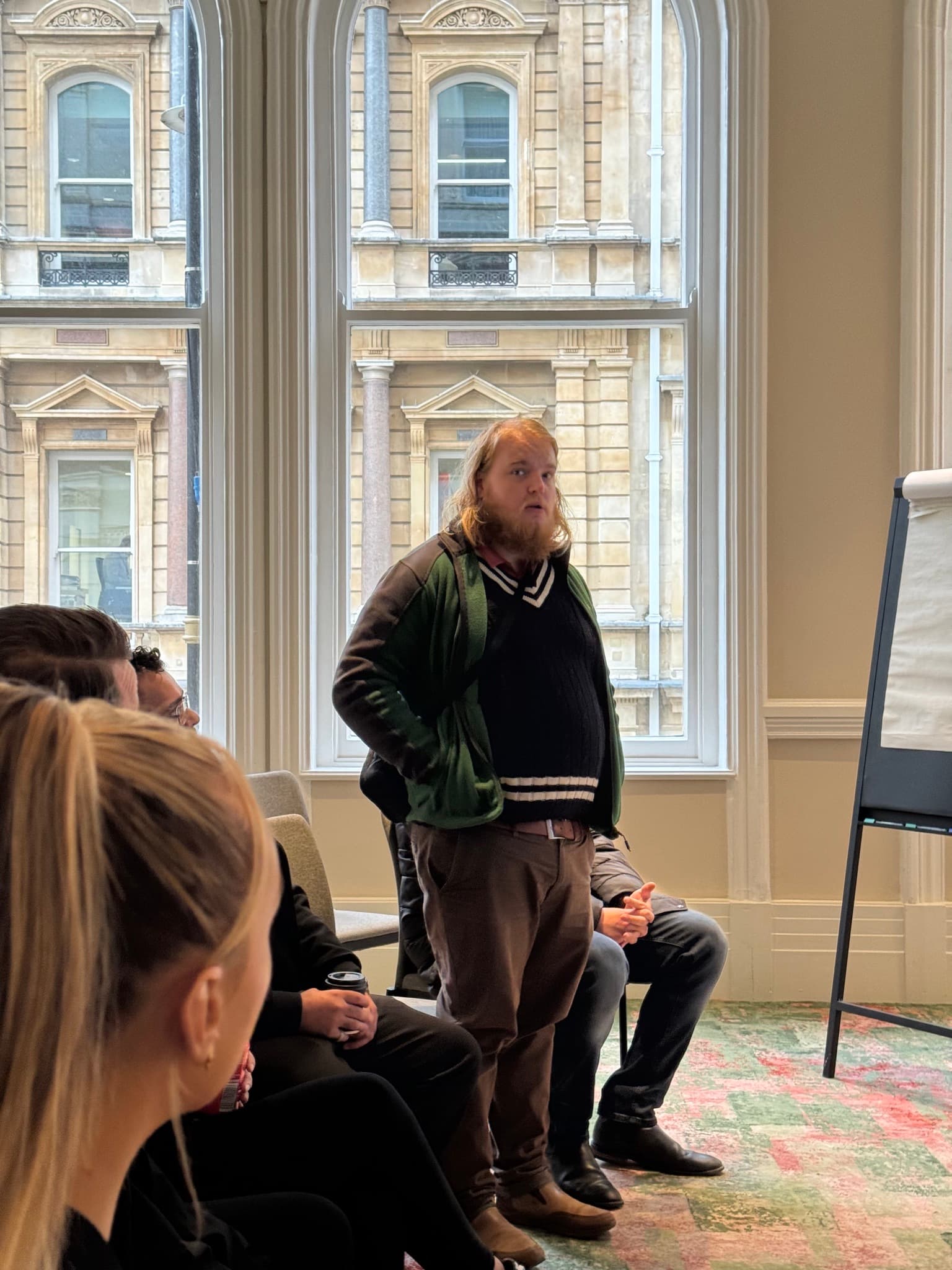 A contributor speaking to a seated group in a workshop room.